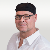 Image is of Achiem. He is wearing square glasses, a white shirt and black hat.