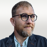 image is of headshot Dominic O'Hooley. He has short brown hair, moustache and beard and round black glasses.