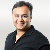 The image is of Nikhil. He has dark hair, a dark shirt and is smiling.