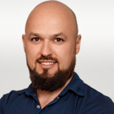 Image is a headshot of Tomas. He is bald with a dark brown beard and moustache. He has dark friendly eyes and is smiling.