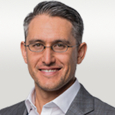 image is of William. He has grey hair swept over, a white shirt and grey blazer and thin framed glasses.